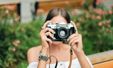 Portrait of young beautiful woman in summer clothes with retro camera takes a picture while sitting...