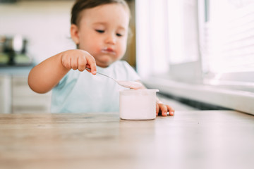 Little girl in the afternoon in the kitchen eating yogurt