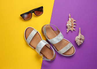 Creative summer beach flat lay. Leather women's sandals, shells, sunglasses on purple yellow background. Top view