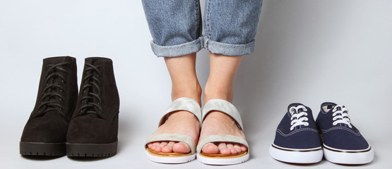 Woman chooses sandals among other seasonal shoes. Female legs in jeans, Sandals, sneakers, boots on...