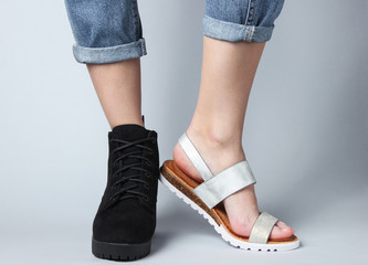 Female legs in jeans shod in boot and sandal on a white background. Seasonal shoes. Creative fashion shot