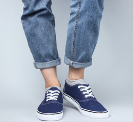 Fashion studio shot. Female legs in jeans and sneakers on a gray background.