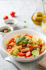 Whole wheat pasta salad with cucumbers, cherry tomatoes, salted salmon and capers on concrete background. Selective focus.