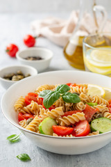 Whole wheat pasta salad with cucumbers, cherry tomatoes, salted salmon and capers on concrete background. Selective focus.