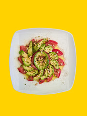 Delicious fresh salad of tomatoes and avocados with pine nuts in yellow background.