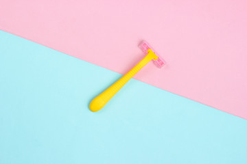Minimalistic beauty concept. Yellow plastic razor on blue pink pastel background. Top view