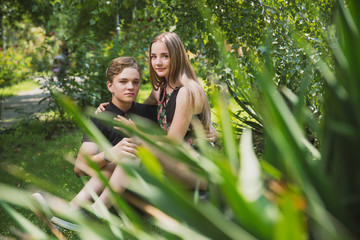 Obraz premium A couple of teenagers in love hugs and poses against the background of flowering trees and shrubs. Young guy and girl on the background of a blooming Park