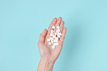 Many white tablets in the palm of hand on blue background. Medical minimalistic concept. Top view