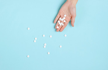 Many white tablets in the palm of hand on blue background. Medical minimalistic concept. Top view