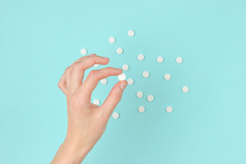 Female hand holding white pills on blue background. Medical minimalistic concept. Top view