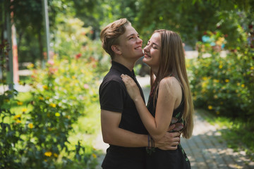 Fototapeta premium A couple of teenagers in love hugs and poses against the background of flowering trees and shrubs. Young guy and girl on the background of a blooming Park