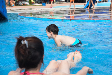 40 Years old Mom play with son in a pool. Cheerful child splashing in the swimming pool with  his mother