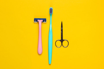 Minimalistic personal care, beauty concept. Plastic razor, toothbrush, nail scissors on a yellow...