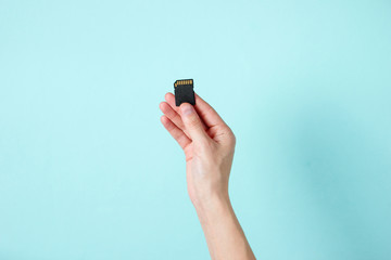 Female hand holds SD memory card on blue background. Minimalist Techno Concept. Top view
