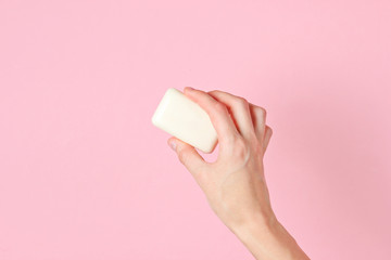 Female hand holding piece of soap against pink background. Top view