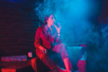 woman smokes a e-cigarette lying on the bed in the room. Smoker's concept Vaping.