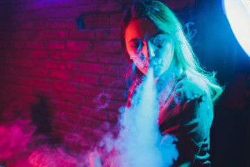 woman smokes a e-cigarette lying on the bed in the room. Smoker's concept Vaping.