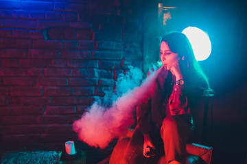 woman smokes a e-cigarette lying on the bed in the room. Smoker's concept Vaping.