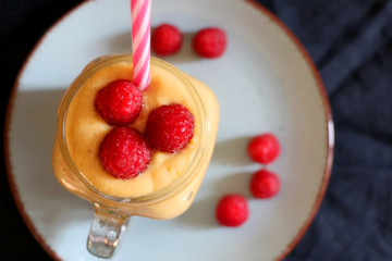 Mango and banana smoothie decorated with raspberries and reusable straw. Top view.