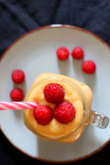 Mango and banana smoothie decorated with raspberries and reusable straw. Top view.