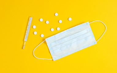 Minimalistic medical still life. flat lay style. Thermometer, pills, gauze mask on a yellow background. Top view
