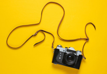 Vintage retro film camera in leather cover with strap on yellow background. Top view