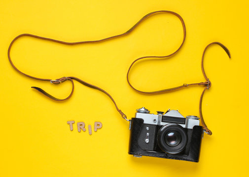 Tourist minimalism concept. Vintage retro film camera in leather cover with strap on yellow background with word trip. Top view