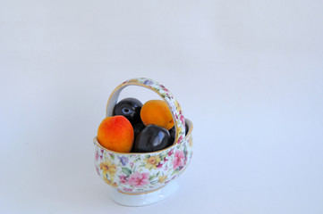 Apricot and plum fruits in a decorative vase for fruits on a white background.