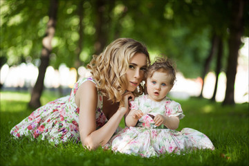 People and family concept - Close up portrait of a mother and little daughter with blue eyes in summer park against a background of green grass and trees