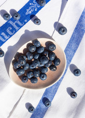 Ripe blueberries on a pink small plate on a white and blue napkin. Top view.