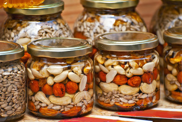 Lots of assorted honey on the table. Jars of sweets are sold at the fair. Honey with different kinds of nuts then dried fruits.