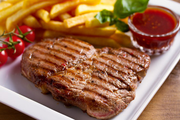 Grilled steak, fries, sauce and vegetables on plate