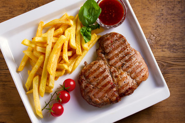 Grilled steak, fries, sauce and vegetables on plate. View from above, top studio shot