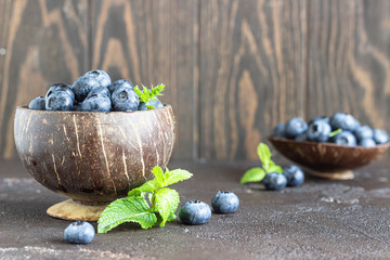 Freshly picked blueberries in wooden bowl. Juicy and fresh blueberries with mint on dark stone background. Blueberry antioxidant. Concept for healthy eating and nutrition. 