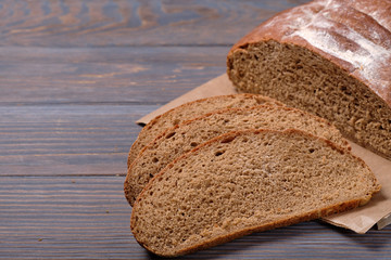 Sliced rustic bread loaf on wooden table. Dark background.