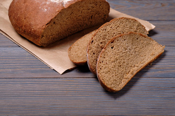 Sliced rustic bread loaf on wooden table. Dark background.