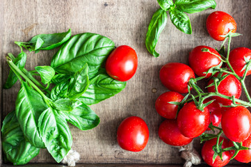 Fresh ripe cherry tomatoes and basil on a wooden background.