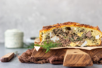 Pie with liver, egg and dill filling on a wooden cutting board. Healthy nutrition lunch or dinner.