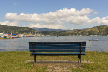 Empty bench facing the sea. Intense blue sky with clouds. Paraty, Brazil. 2018