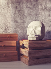 A decorative figure in the form of a human skull is on a pile of books inside a wooden box. Nearby...