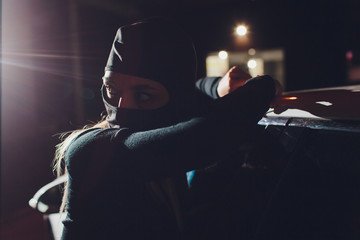 Masked robber woman car The thief is levering the lock at the door car robbery.