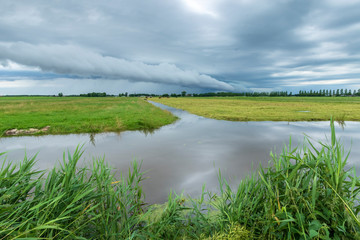 Shelf cloud and thunderstorm passing above green farmland and water