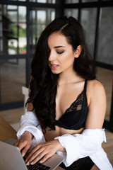 Naklejka premium sexy girl in black underwear and white shirt using laptop with closed eyes