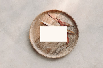 Blank white business card mockup on wooden plate. Marble backgound with dry colorful eucalyptus leaves. Modern template. Branding identity. Natural autumn, fall design. Flat lay, top view.