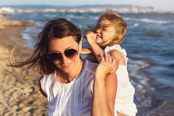 Happy mom and daughter playing with each other on the seashore on a warm sunny evening