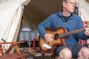 Obraz premium Man relaxing and enjoying some peaceful time playing guitar at the campsite