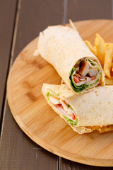 Wrapped sandwich chicken tortilla with fried potatoes and dipping sauce on wooden plate , wood background.
