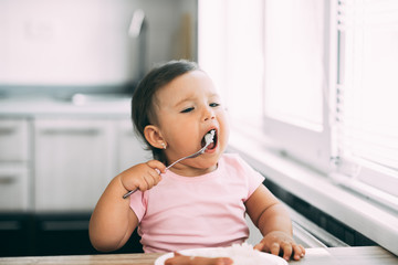Little baby girl in the kitchen eating sausage and mashed potatoes