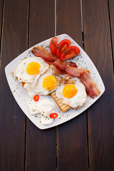 Healthy bacon fried egg on toast bread breakfast on plate , fresh tomatoes and cheese on plate , wood background.