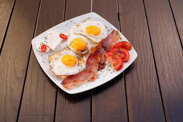 Healthy bacon fried egg on toast bread breakfast on plate , fresh tomatoes and cheese on plate , wood background.
